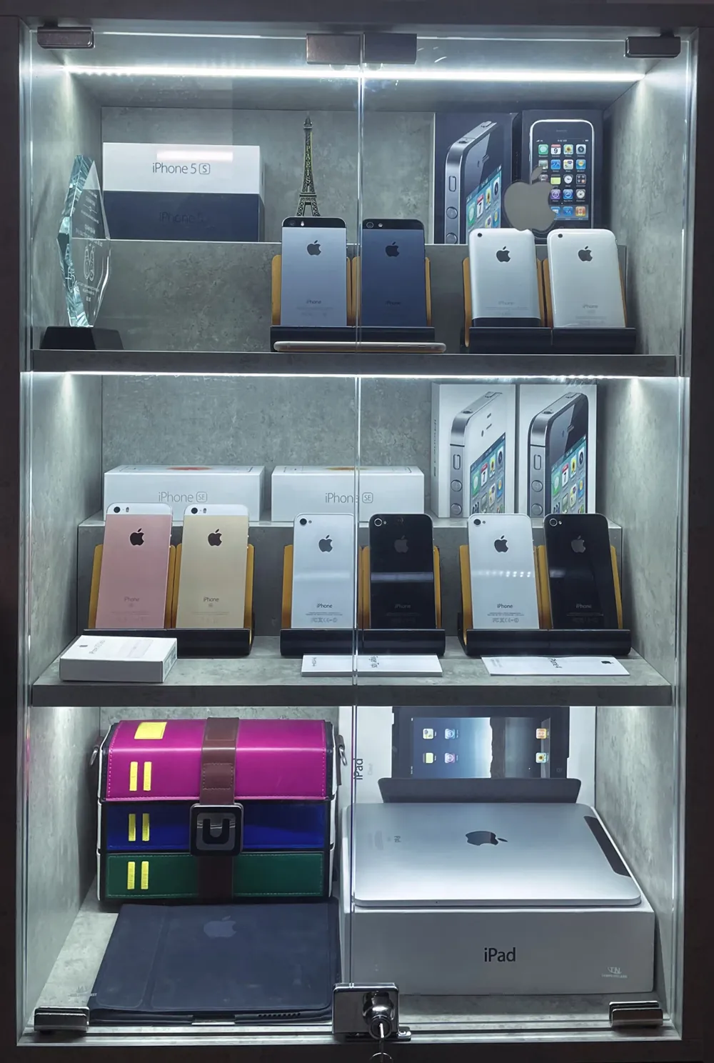 The whole cabinet from the front: iPhones and their boxes on two shelves, and an iPad with its box on the bottom shelf.